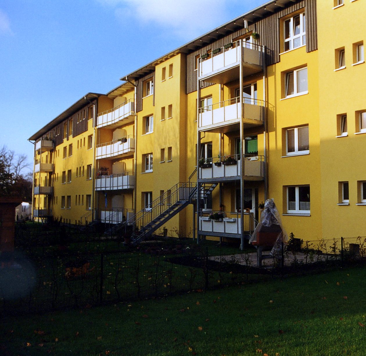 Sanierte Wohnanlage mit gelber Fassade, Balkonen und außen liegendem Treppenaufgang