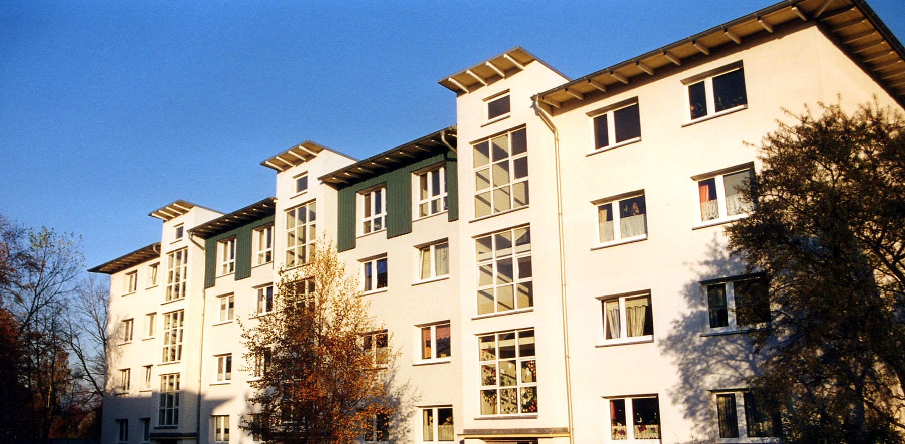 Saniertes Mehrfamilienhaus mit hellem Putz, grünen Giebelflächen und Treppenhausfenstern