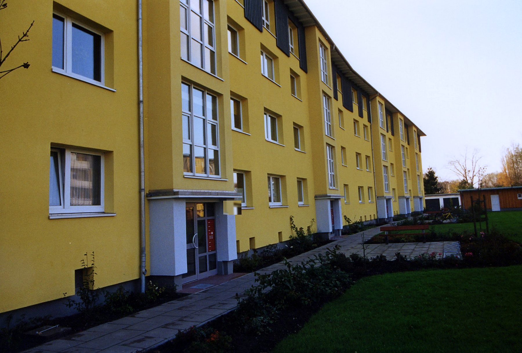 Sanierte Wohnzeile mit gelber Fassade, neuen Hauseingängen und angelegten Außenanlagen